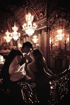 a man and woman kissing in front of a chandelier