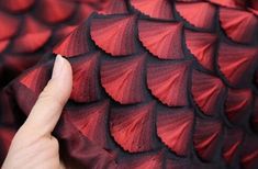 a hand is touching the red and black material on a dragon skin pattern, which looks like scales