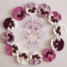 crocheted flowers arranged in a circle on a white surface with yellow and purple centers