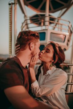 a man and woman kissing each other in front of a ferris wheel