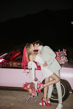 a man and woman kissing in front of a pink car