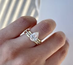 a woman's hand wearing a gold ring with a pear shaped diamond on it