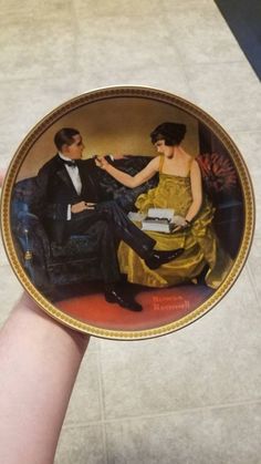 a hand holding a plate with an image of a man and woman sitting on a couch