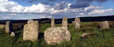 several large rocks sitting in the middle of a grassy field under a cloudy blue sky