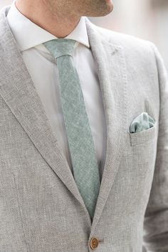 a man wearing a gray suit with a light green tie and buttoned up shirt