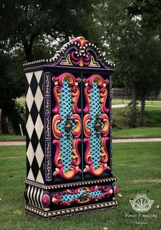 an elaborately painted cabinet in the middle of a park with trees and grass behind it