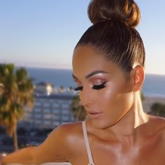 a woman with black eyeliners is looking down at her cell phone while standing near the ocean