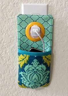 a cell phone holder with a yellow and blue flower design on the front, attached to a white wall