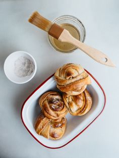 some cinnamon rolls are on a plate next to a bowl of powder and a brush