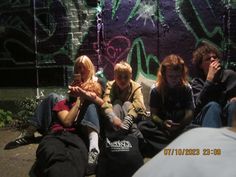 four people sitting on the ground in front of graffiti