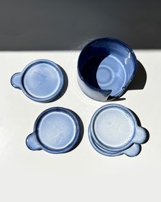 three blue cups sitting on top of a white table next to a cup and saucer