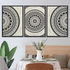 three black and white paintings on the wall above a table with flowers in a vase