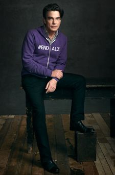 a man sitting on top of a wooden bench wearing a purple sweater and black pants