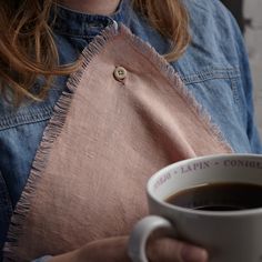 a close up of a person holding a cup of coffee and wearing a denim jacket