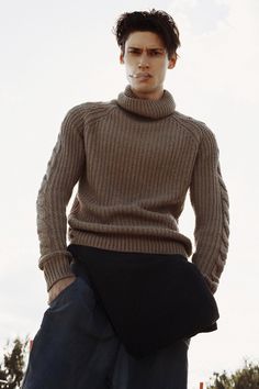 a man in a turtle neck sweater is standing with his hands on his hips