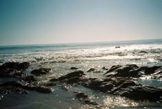 the sun shines on some rocks in the water at the beach near the ocean