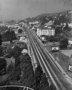 black and white photo of an old town with lots of traffic on the road in front of buildings