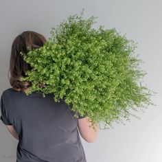 a woman holding a bunch of green plants in front of her face and behind her head