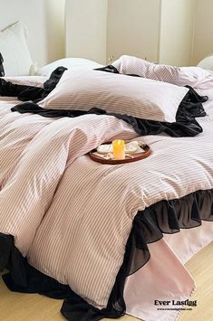 an unmade bed with pink and black ruffled bedspread, candle and pillows