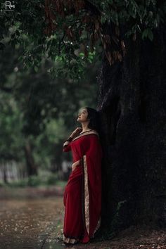 a woman in a red sari leaning against a tree with her hands on her hips