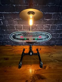 a table lamp sitting on top of a wooden floor next to a brick wall with a light bulb over it