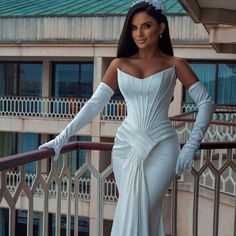 a woman in a white dress standing on a balcony with her hands on her hips