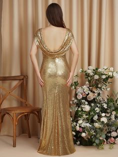 a woman in a gold sequinned gown standing next to a chair and flowers