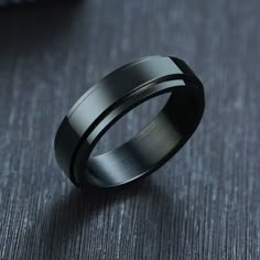 a black ring with silver inlays sits on a gray surface next to a plant