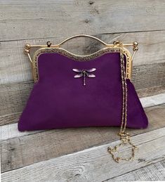 Stunning, handmade, purple velvet clutch bag with dragonfly detail. The lining is made with a beautiful fabric. Use it as a classic clutch or attach the shoulder strap to wear over your shoulder or as a crossbody. - Gold colour Chain strap (detachable) - Gold colour Kiss clasp (20.5cm) - Rhinestone dragonfly (not detachable) - H:21.5cm (handle not included) x W:29.5cm x D:5cm approximately The pattern of the lining inside of the bag may vary. But don't worry, I always make sure the lining of the Elegant Purple Bag Gift, Elegant Purple Clutch For Everyday Use, Purple Pouch Evening Bag As Gift, Elegant Purple Clutch For Daily Use, Elegant Purple Handheld Bag, Elegant Purple Evening Bag, Elegant Purple Pouch Shoulder Bag, Elegant Purple Clutch Bag, Purple Pouch Clutch As Gift