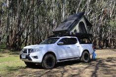 a white pick up truck with a tent on the roof parked in front of trees