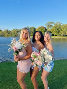 three beautiful young women standing next to each other in front of a body of water