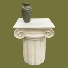 a green vase sitting on top of a white pedestal