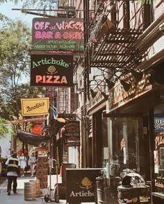 people are walking down the street in front of some shops and restaurants with neon signs