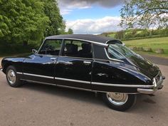 an old black car is parked on the side of the road in front of some trees