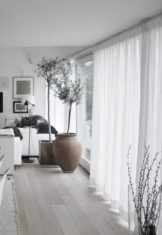 a living room filled with white furniture and large vases on the floor next to windows