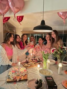 a group of women standing around a table with food and drinks in front of them