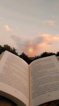 an open book sitting on top of a wooden table next to a tree filled field