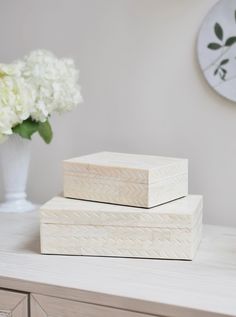 two wooden boxes sitting on top of a white table next to a vase with flowers