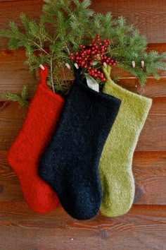 three christmas stockings hanging from a tree on a wooden wall with berries and pine needles