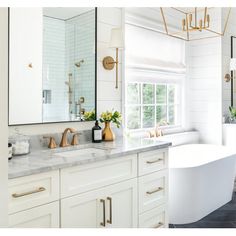 a white bathroom with gold accents and marble counter tops, along with an oval bathtub