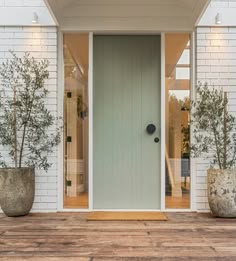 two large planters on the outside of a white brick building with a green door