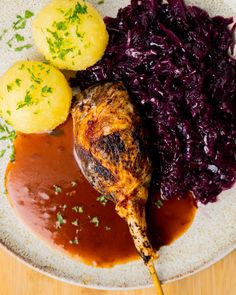 a white plate topped with meat, potatoes and red cabbage covered in gravy