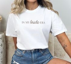 a woman sitting on a couch wearing a white t - shirt that says in my bride era