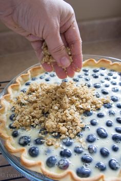 a person is sprinkling blueberries with oatmeal in a pie pan