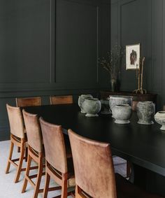 a dining room table with chairs and vases on it in front of dark green walls