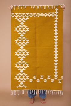 a woman standing in front of an orange and white rug with fringes on it