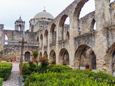 an old stone building with arches in the middle and flowers growing on the ground next to it