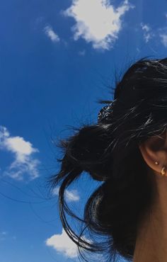 a close up of a woman's ear with sky and clouds in the background