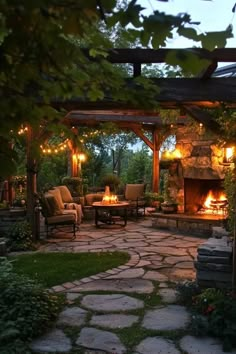 a stone patio with fire pit and seating area at night, surrounded by greenery