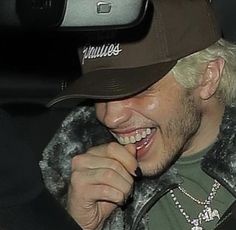 a man with blonde hair wearing a brown hat and smiling while sitting in a car